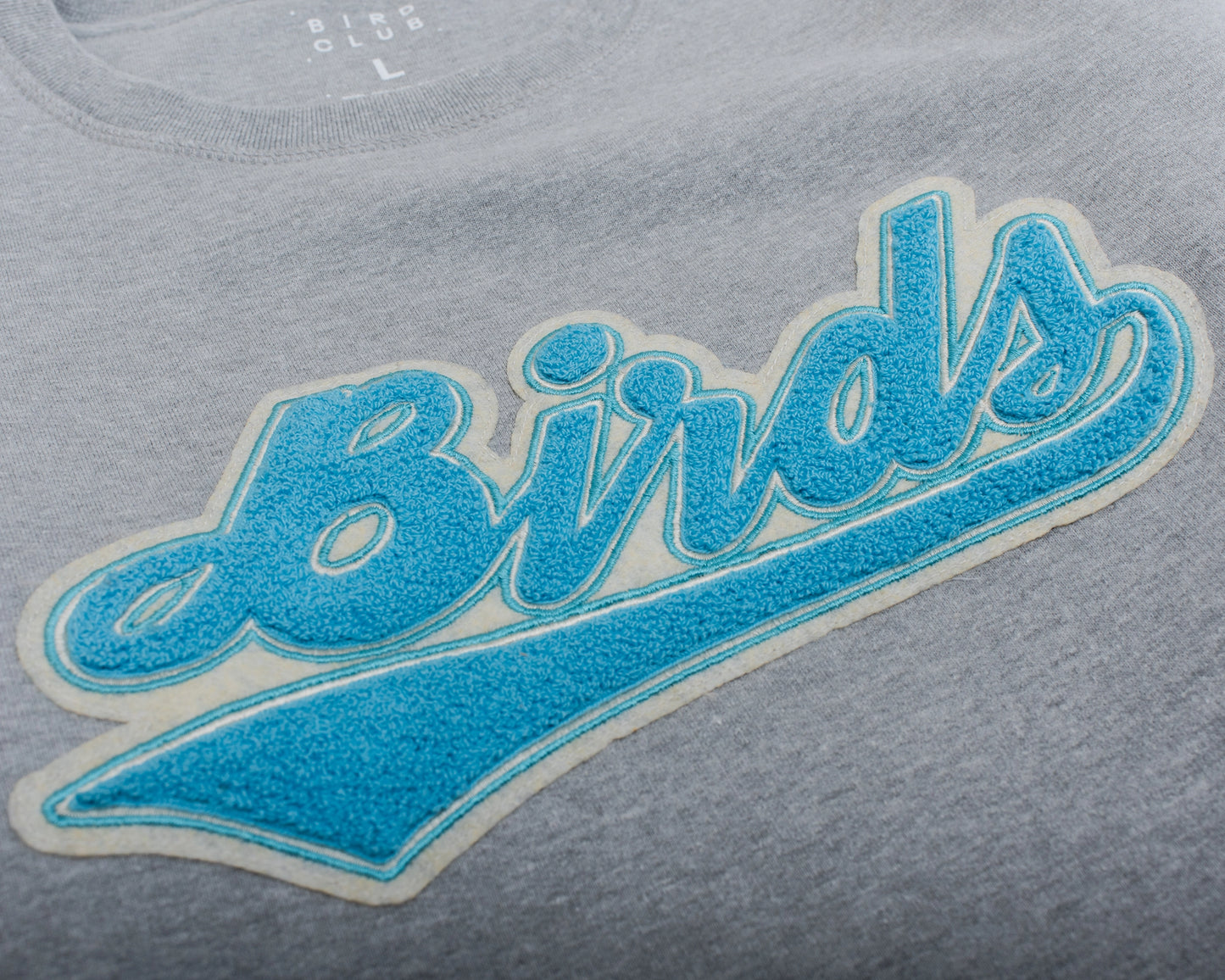 Close-up of a Bird Club sweatshirt featuring chenille embroidery of the word 'Birds' in blue, framed to highlight the detailed texture and quality of the design. Birds Script birding-inspired Crewneck