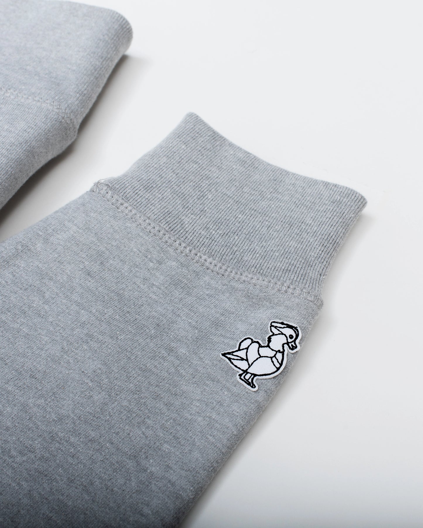 A detail of the black and white BIRD CLUB mandarin duck logo. It's stitched onto the wrist in a way that when you hold up binoculars you see the image correctly. Sleeve of the heather grey Birds Script Crewneck. 