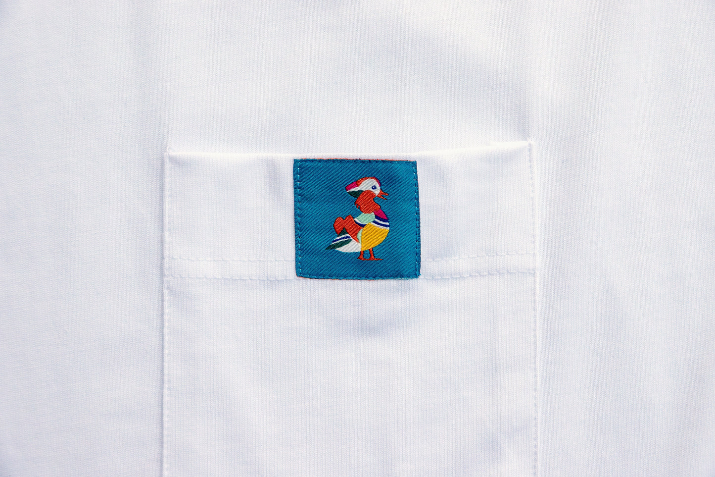 Close-up of the woven Mandarin Duck Logo label on the pocket of an organic cotton ornithology t-shirt, perfect for gifts for birders or bird watcher gifts.