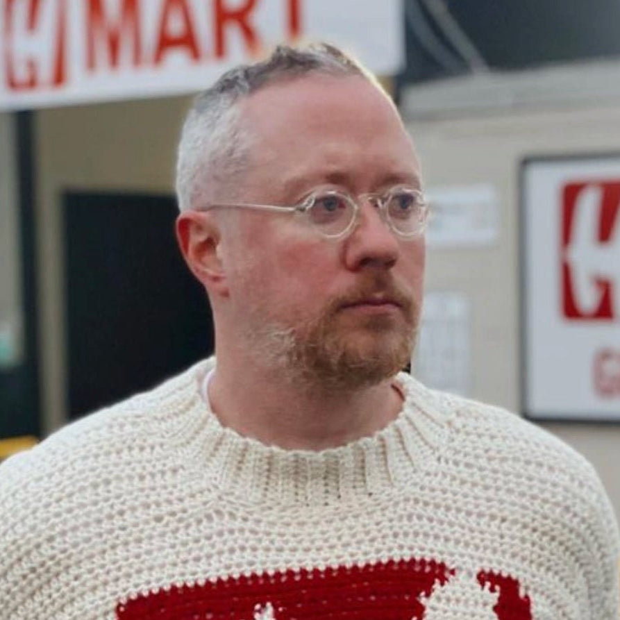 Brendan Kennedy stands in front of H-Mart, wearing the viral H-Mart sweater that he hand knit. . This image highlights his connection with knitting and the sustainable brand BIRD CLUB, known for its commitment to eco-friendly practices and promoting a naturalist lifestyle.