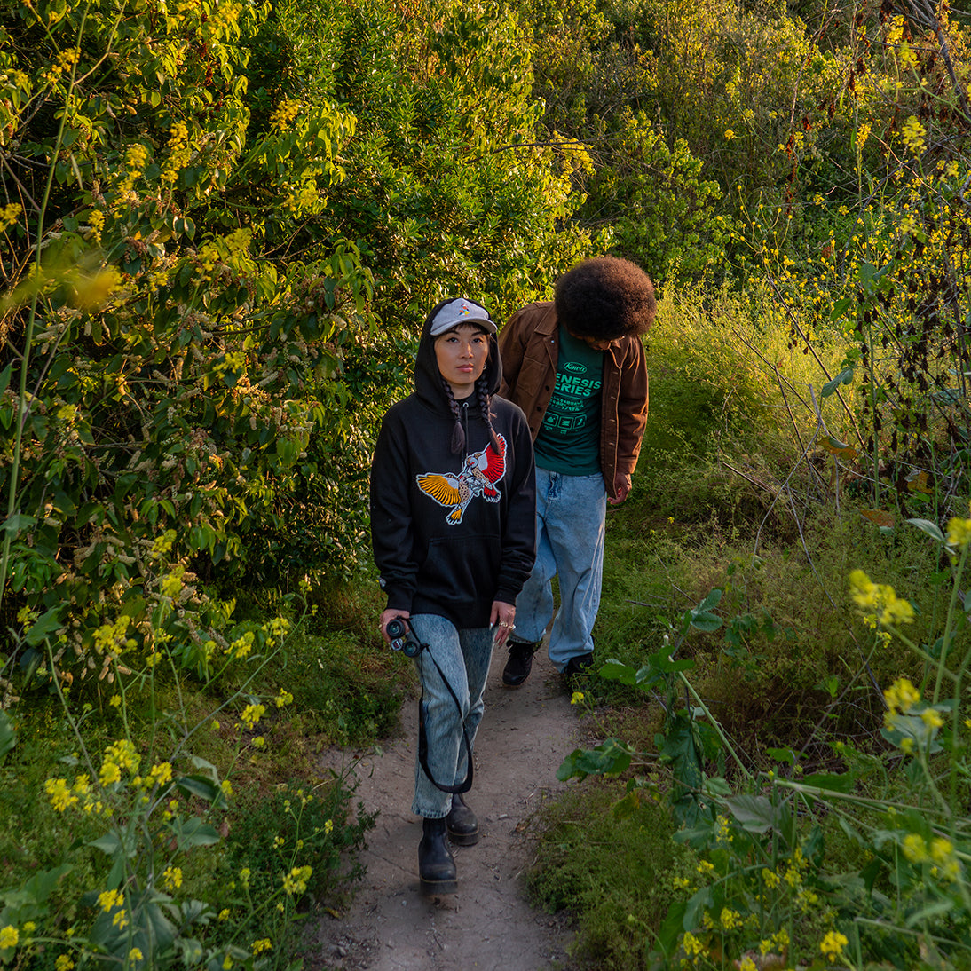 Two individuals walking through nature wearing Bird Club apparel, with the person in front sporting a bird hoodie featuring a vibrant bird design. Ideal for those searching for bird watcher gifts or gifts for birders, this stylish hoodie is a great choice for eco-conscious bird enthusiasts who love connecting with nature.