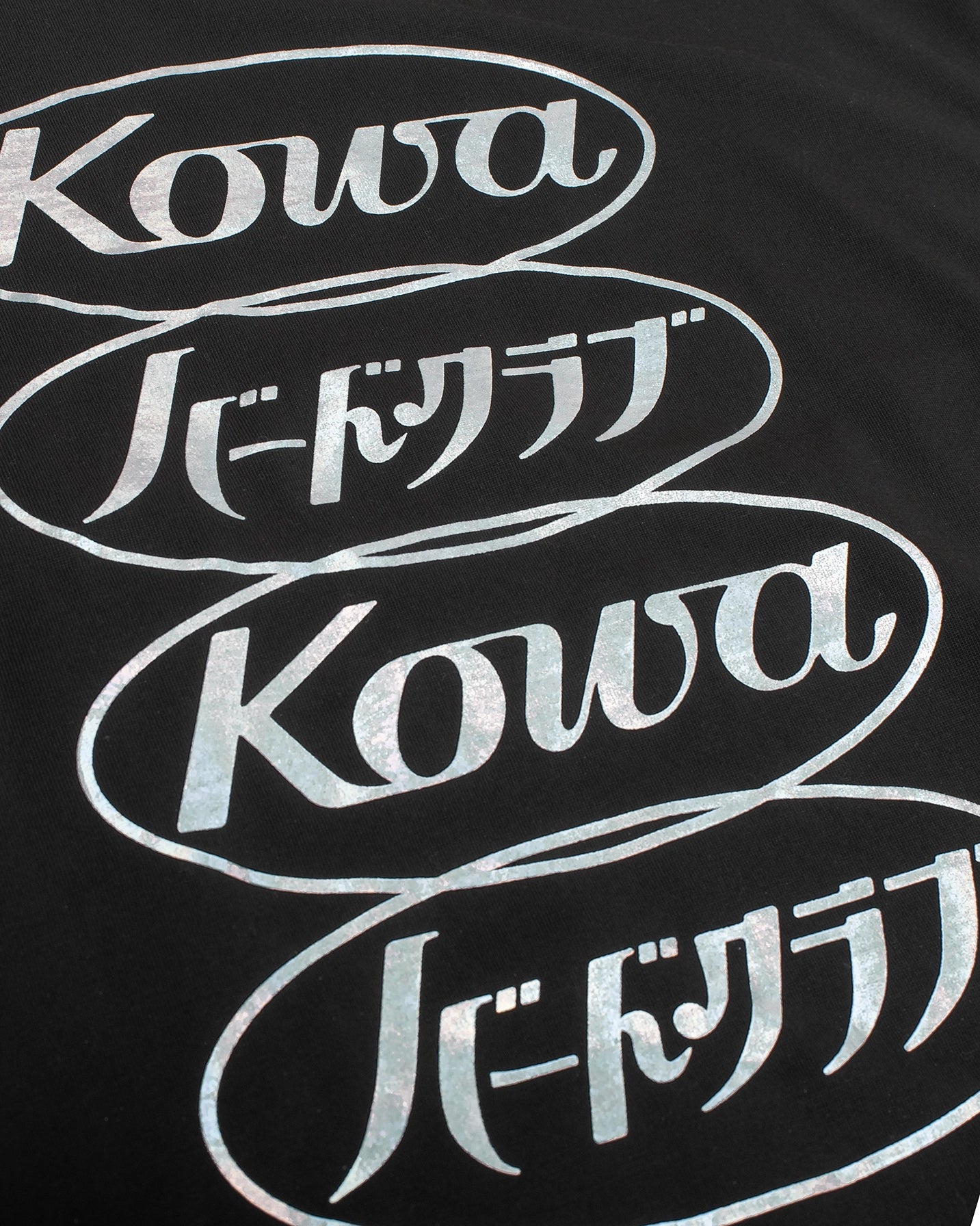 A detail of the art on the chest of the Visionary Long-Sleeve Tee from BIRD CLUB. Four interlocking ovals stacked vertically say Kowa, BIRD CLUB (in Japanese), Kowa, and BIRD CLUB (in Japanese). 